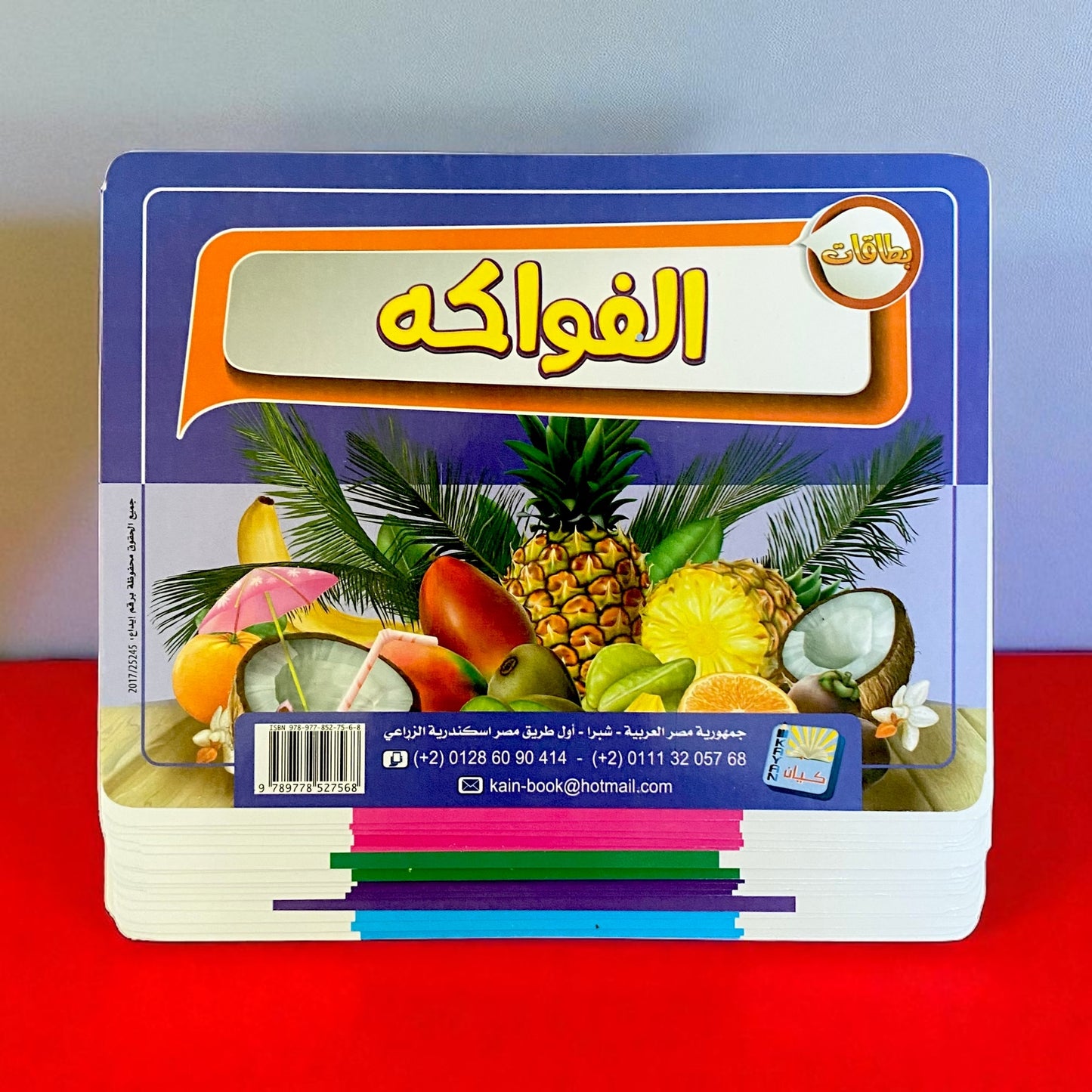 Stack of colorful books with fruit illustrations on a red surface