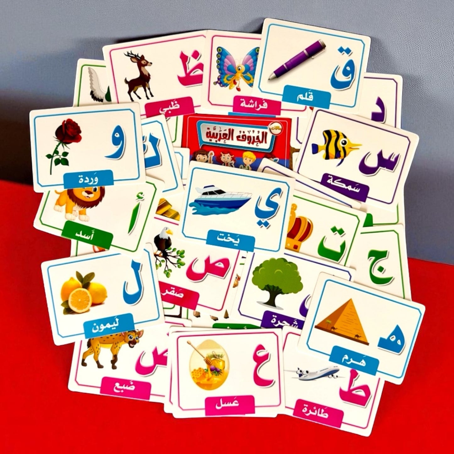 Educational Arabic language flashcards on a red surface with a gray background