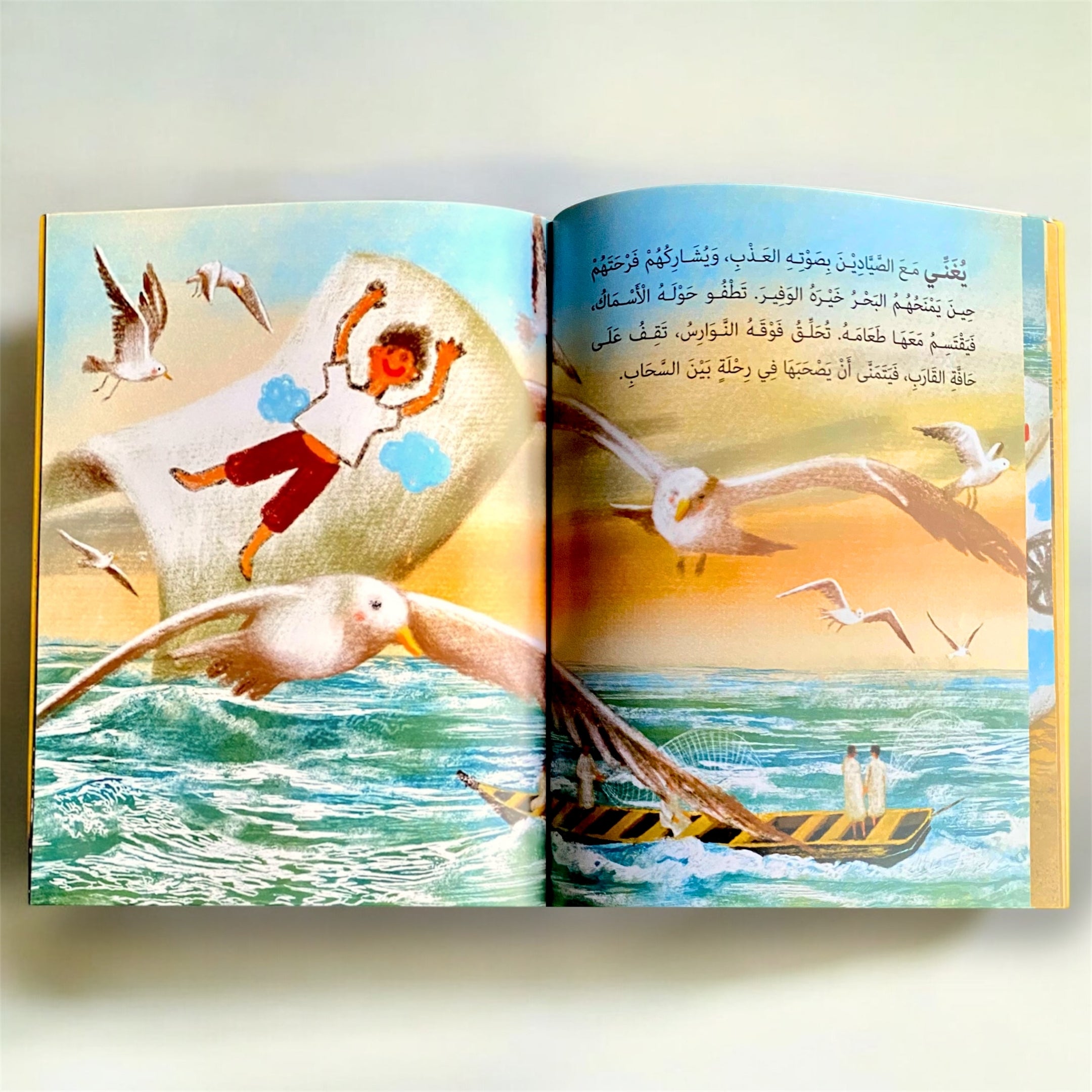Open book with illustrations of a child on a pillow, seagulls, and a boat on a beach.