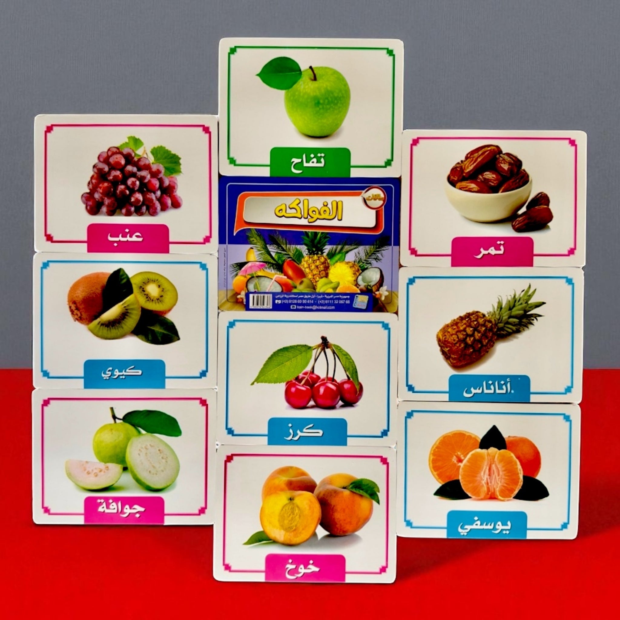 Educational card set with images of fruits and their names in Arabic on a red and gray background.