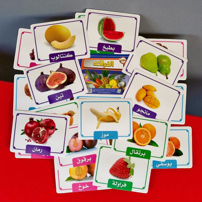 Educational cards with images of fruits and their names in Arabic on a red surface.